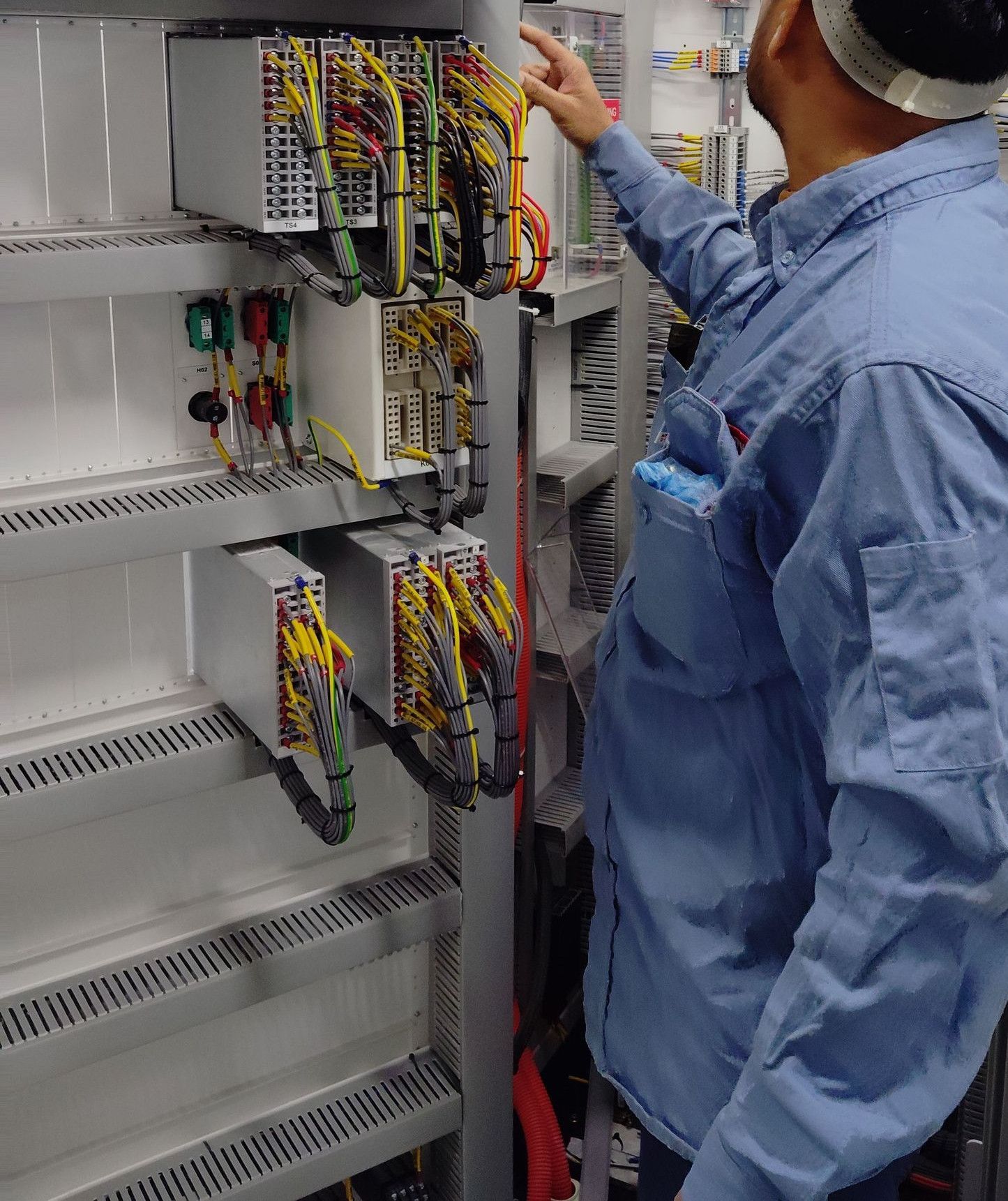 An electrician in a hard hat inspecting a control panel inside an industrial setting, ensuring safety and functionality.
